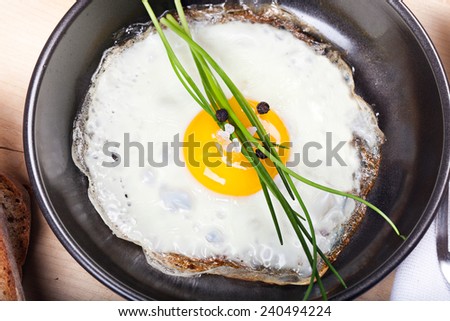 fried egg sunny side up with parsley, salt, pepper, bread, in frying pan on wooden plate
