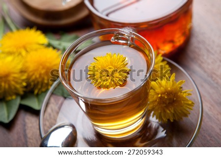 dandelion herbal tea with yellow blossom inside, honey and leaf on wooden table
