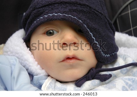 Baby boy in winter outfit with one eye closed by a hat