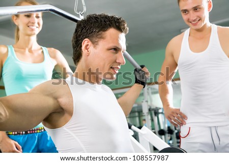 Fitness. Yung man at the gym doing arms exercises on a machine