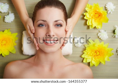 Beautiful young woman lying relaxed in a spa salon and receiving facial massage. Beauty treatment.