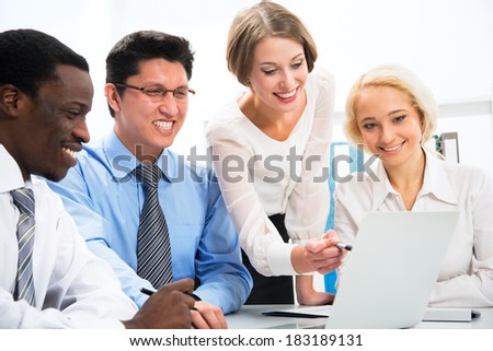 Happy business people gathered around laptop looking at monitor in the office