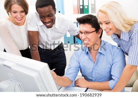Happy business people gathered around laptop looking at monitor in the office