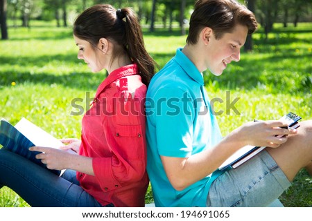 Two students studying in park on grass with outdoors