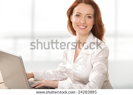 Beautiful businesswoman sitting in office before laptop and looking at camera