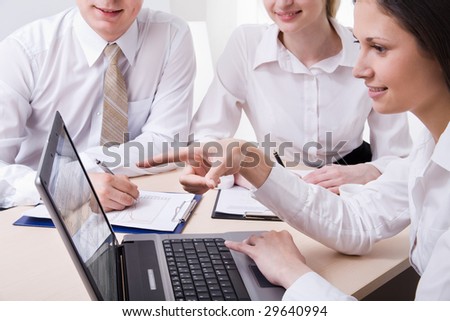 Two businesswomen and a businessman sitting with opened laptop, documents and discussing questions