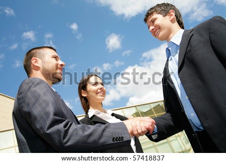 Young and successful businesspeople shake hands against the sky