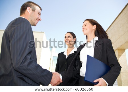 Young and successful businesspeople shake hands against the modern office building