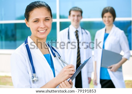 Portrait of a female doctor with two of her co-workers against modern hospital building