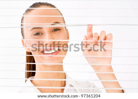 Happy business woman peeking through a venetian blind in an office