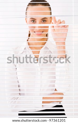 Happy business woman peeking through a venetian blind in an office