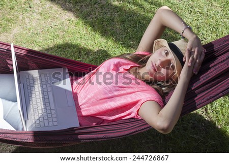 Woman with computer sitting in hammock on sunny day