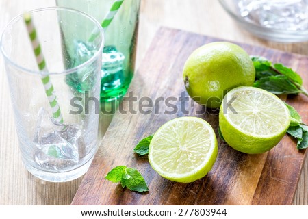 Fresh juicy limes, mint leaves and a cocktail stick on a wooden cutting board