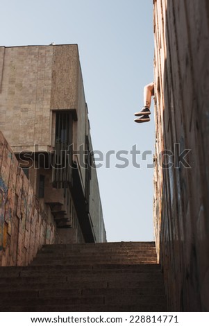 Feet in sneakers. Human legs hanging from wall in middle of city