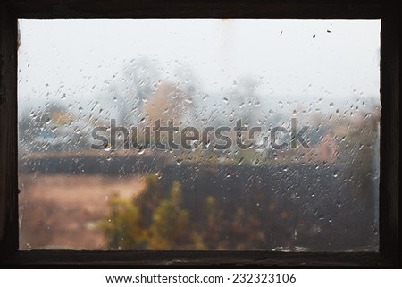 Rain drops on glass in frame. Texture of glass. Rainy weather. Sad autumn mood. Rural landscape outside window