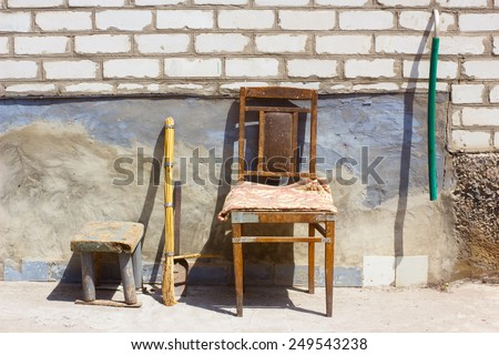 Chair, stool, broom, hose and scoop. Still life with household items. Old wooden furniture. Brick wall