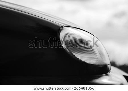 Car headlight. Fragment of car with headlight and reflections on hood. Black and white photo