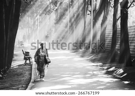 Woman in Park. Elderly lady carrying water bottle in morning sun. Beautiful sun rays. Black and white photo