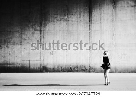 Girl and her shadow. Girl holds fluttering from wind dress. Female long shadow. Street scene. Black and white photo