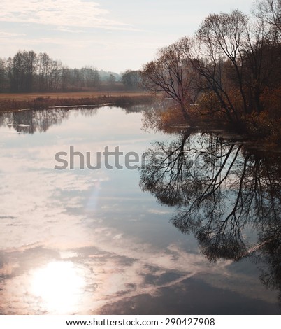 Landscape with river. Trees on banks of river reflected in water. Sunny morning. Reflection of sky in water