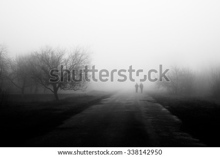 Wayfarers in fog. Silhouette of friends walking on misty village road. Homecoming. Loneliness, nostalgia, sad mood. Black and white photo