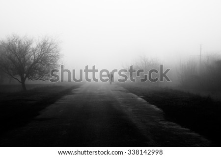 Wayfarer in fog. Silhouette of man walking on misty village road. Homecoming. Loneliness, \nostalgia, sad mood. Black and white photo