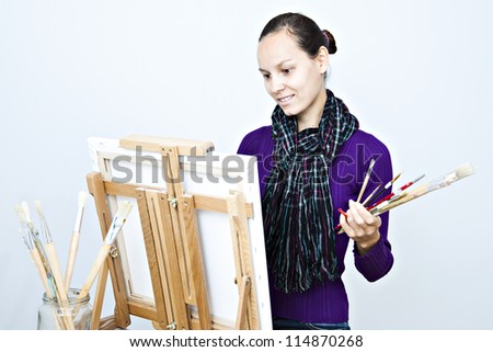 Artist sitting in front of easel with brushes in her hands