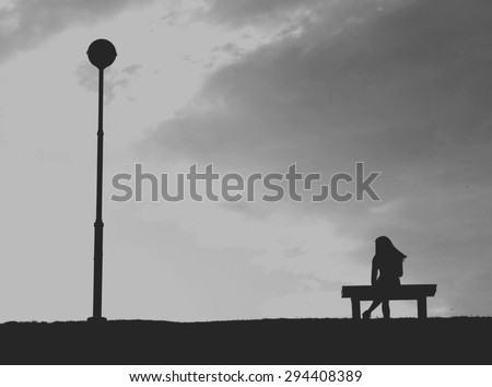 The silhouette of woman sitting alone with grey sky, concept of lonely, sad, alone, person space