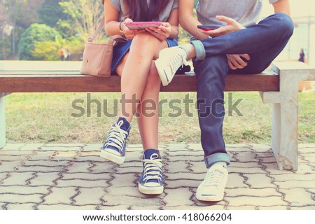 Close up of hipster couple in disinterest moment with smart phones in the outdoor, concept of relationship apathy and isolating using new technology and smartphone addiction