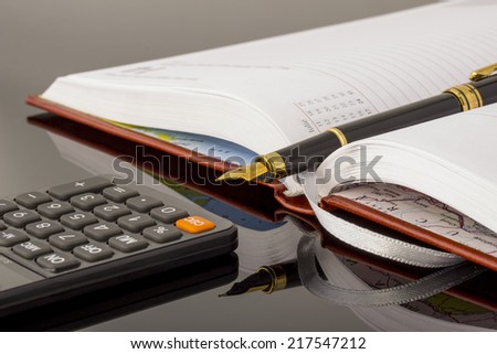 Pen on notebook sitting near the calculator on black glass
