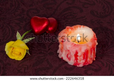 Red hearts chocolate, yellow rose and lit candle on velvet background