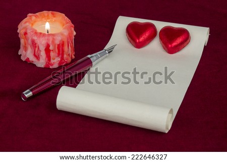 Red chocolate hearts set on white paper with a pen and a lit candle on red velvet background