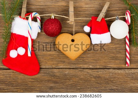 Christmas decoration - red sock gift, gingerbread heart, globes, candy cane, rope with wood hooks and fir branches on old wooden background