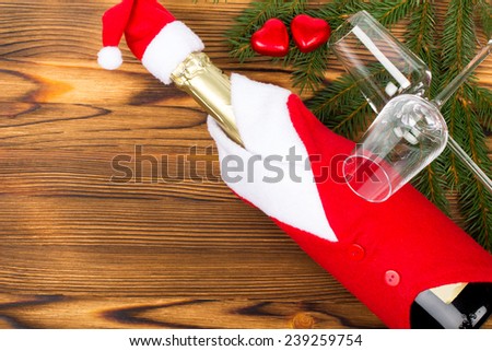Winter holidays decoration - glasses and bottle of champagne wearing red clothes and hat, red hearts on fir branches on old wooden background