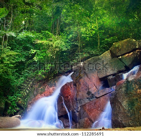 Waterfall landscape in tropical forest. Jungle background with green trees and mountain river.