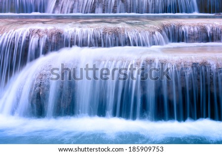 Mountain river background with small waterfalls in tropical forest. Clean blue water flows on cascades of Erawan park in Thailand