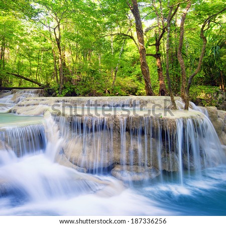 Waterfall landscape background. Beautiful nature outdoor photography. Thailand green rain forest jungle with trees and bushes, fresh clean and cool water river flows through stones cascades and roots
