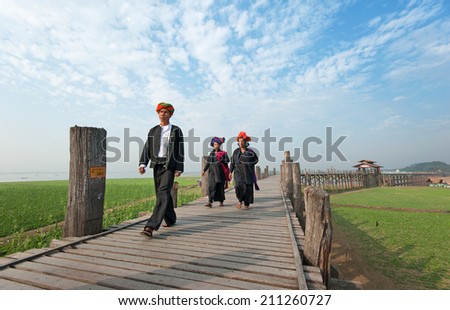 MANDALAY, MYANMAR - JAN 19, 2014: Unidentified group of people from Burmese ethnic minority crossing U Bein bridge. The place is known as one of most honored among citizens of Burma