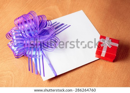Close up of a note card with violet bow and red gift box on wooden background