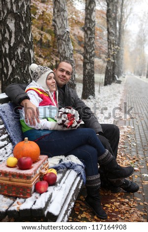 Young man and woman sitting on a bench in the snow-covered park.