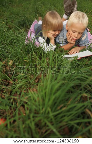 blond 6-year-old boy and 4-year-old girl reading a book lying on the grass. Copy space