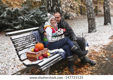 Young man and woman sitting on a bench in the snow-covered park.