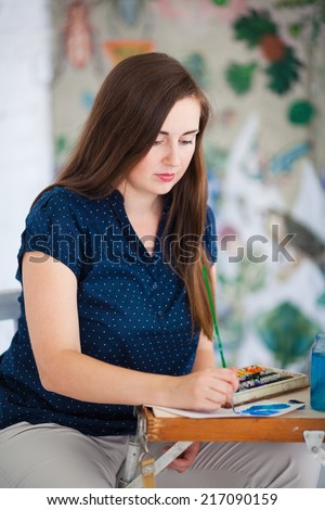 Artist painting picture on canvas with watercolors in her white studio