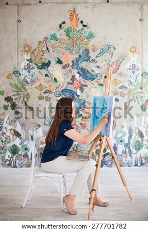 Artist painting picture on canvas whith watercolours in her white studio