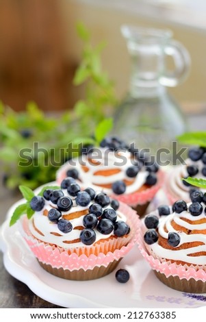 Cupcakes decorated with butter cream and fresh berries in polka dot cases on wooden background