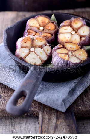 Fresh garlic roasting in olive oil in a pan on an old vintage cutting board.  Selective focus