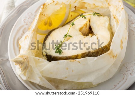 Cod fillets  baked in parchment paper with slices of lemon and a sprig of thyme on light dishes. Selective focus. Concept of healthy food.