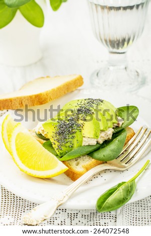 delicious sandwich of toasted bread, avocado and spinach, with chicken, sprinkle with poppy seeds on a white plate and white vintage tablecloth. Served with lemon slices. selective Focus