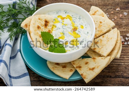 Sauce with yogurt and cucumber for starter with slices of bread on a white plate and a dark natural wood background. selective Focus