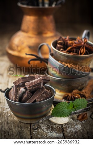 Dark chocolate, vanilla, vanilla sugar, cocoa powder, aniseed wearing vintage silver cups on a wooden natural background with a coffee pot in the background. selective Focus
